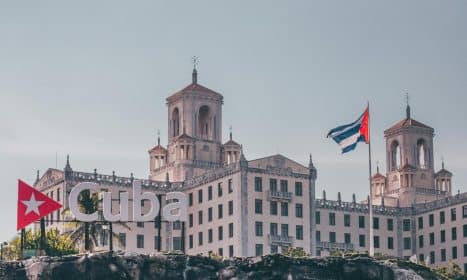 View of the historic Hotel Nacional in Havana, Cuba with a waving Cuban flag and clear sky.