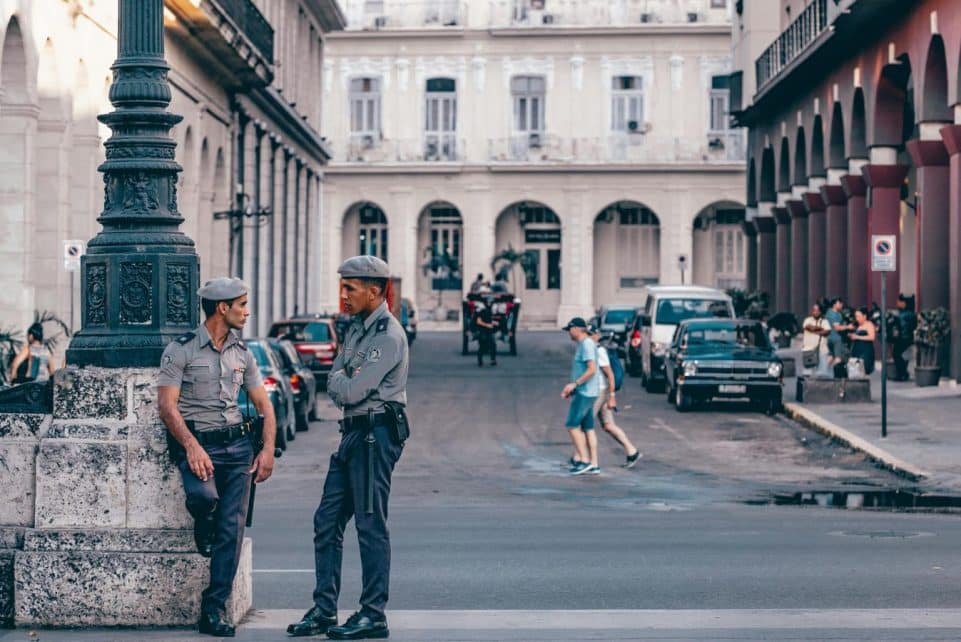 Police officers conversing in a scenic Havana street, showcasing historic architecture.