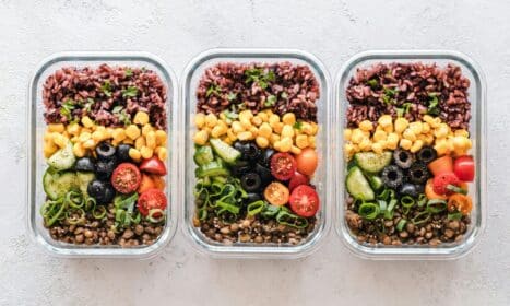 Colorful healthy meal prep with corn, olives, tomatoes, and lentils in glass containers. Perfect for mindful eating.