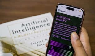 Close-up of a smartphone displaying ChatGPT app held over AI textbook.