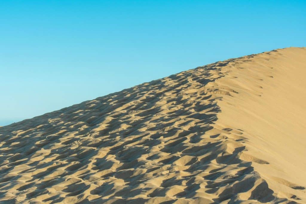Expansive sand dune under a clear blue sky, depicting arid and tranquil desert landscape.