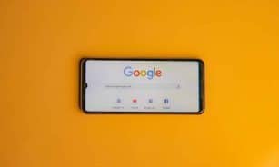 Smartphone displaying Google search page on a vibrant yellow background.