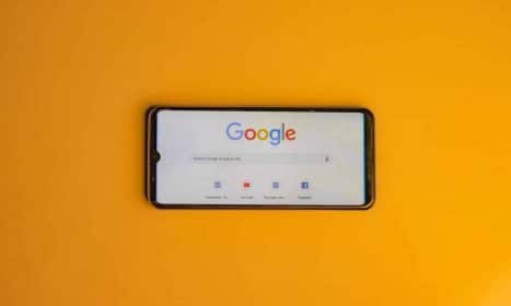 Smartphone displaying Google search page on a vibrant yellow background.