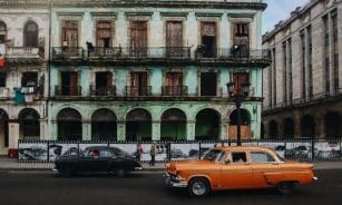 Classic cars passing by a decaying historic building in Havana, Cuba, showcasing vintage urban charm.