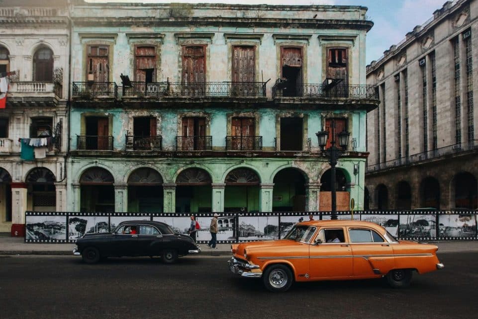 Classic cars passing by a decaying historic building in Havana, Cuba, showcasing vintage urban charm.