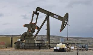 Oil pump jack and equipment at remote industrial site under cloudy sky.