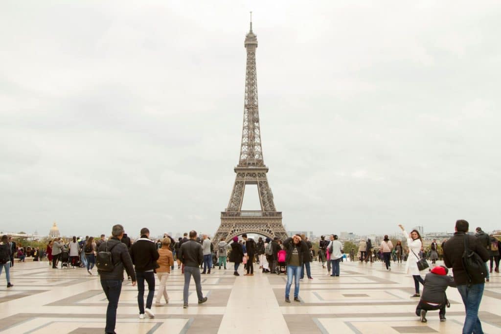 Crowd of tourists at the iconic Eiffel Tower in Paris on an overcast day.