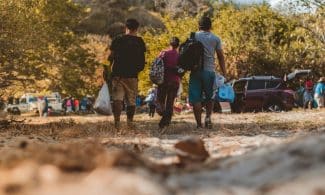 A group of young adults walking towards a gathering in nature, enjoying a sunny day.