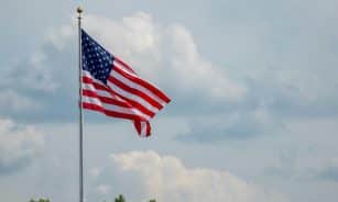 American flag waving on a flagpole, set against a clear blue sky and clouds, symbolizing patriotism.