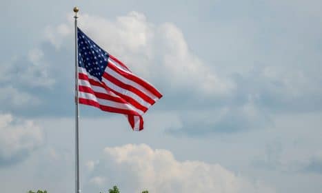 American flag waving on a flagpole, set against a clear blue sky and clouds, symbolizing patriotism.