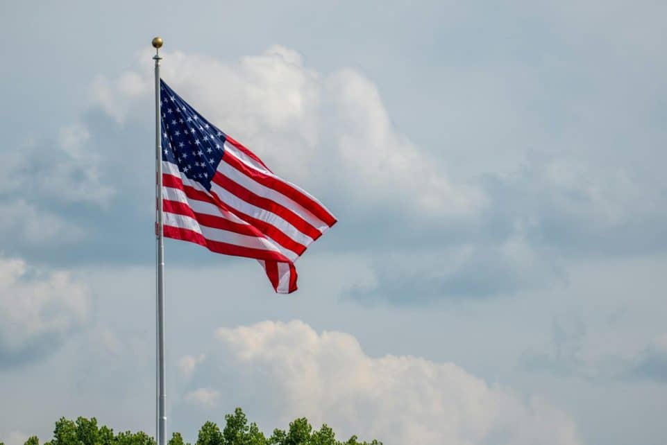 American flag waving on a flagpole, set against a clear blue sky and clouds, symbolizing patriotism.