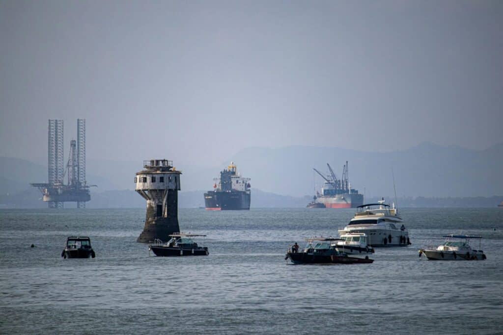 A scenic view of various ships and a tower in Mumbai harbor, India, with an oil rig in the background.