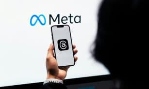 Hands holding smartphone with Meta Threads logo on screen, Meta branding in background.