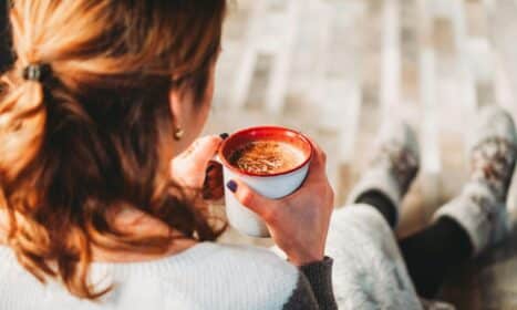 A woman sits comfortably indoors, holding a warm cup of coffee, perfect for a cozy break.