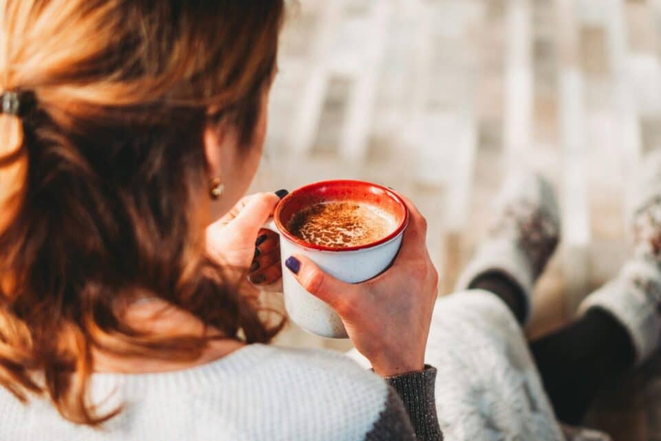 A woman sits comfortably indoors, holding a warm cup of coffee, perfect for a cozy break.