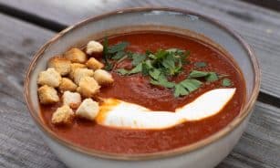 A bowl of creamy tomato soup garnished with croutons and fresh parsley.
