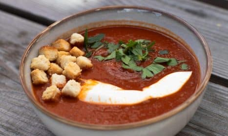 A bowl of creamy tomato soup garnished with croutons and fresh parsley.