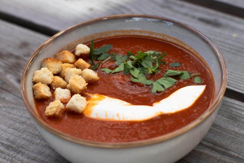 A bowl of creamy tomato soup garnished with croutons and fresh parsley.