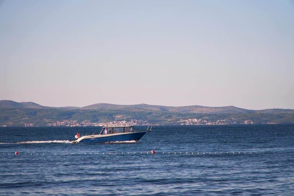 A motorboat speeds across the tranquil ocean with distant hills in the background, under clear skies.