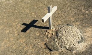 A solitary wooden cross casting a shadow on an arid grave site, symbolizing solitude and spirituality.