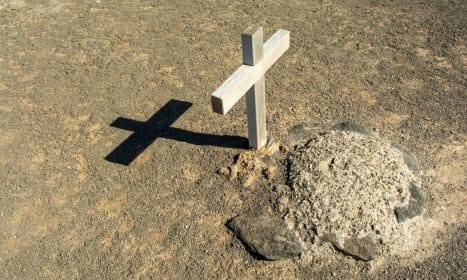 A solitary wooden cross casting a shadow on an arid grave site, symbolizing solitude and spirituality.