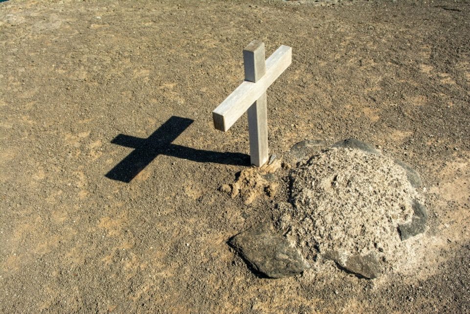A solitary wooden cross casting a shadow on an arid grave site, symbolizing solitude and spirituality.