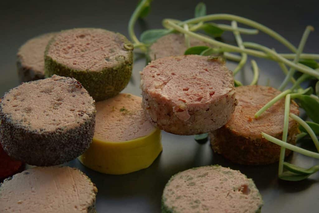 Close-up of various gourmet pâtés, each with a unique seasoning, presented on a slate surface.