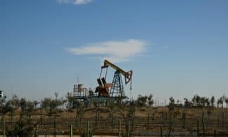 Oil pump jack in a dry landscape with shrubs and clear sky in Bakú, Azerbaijan.