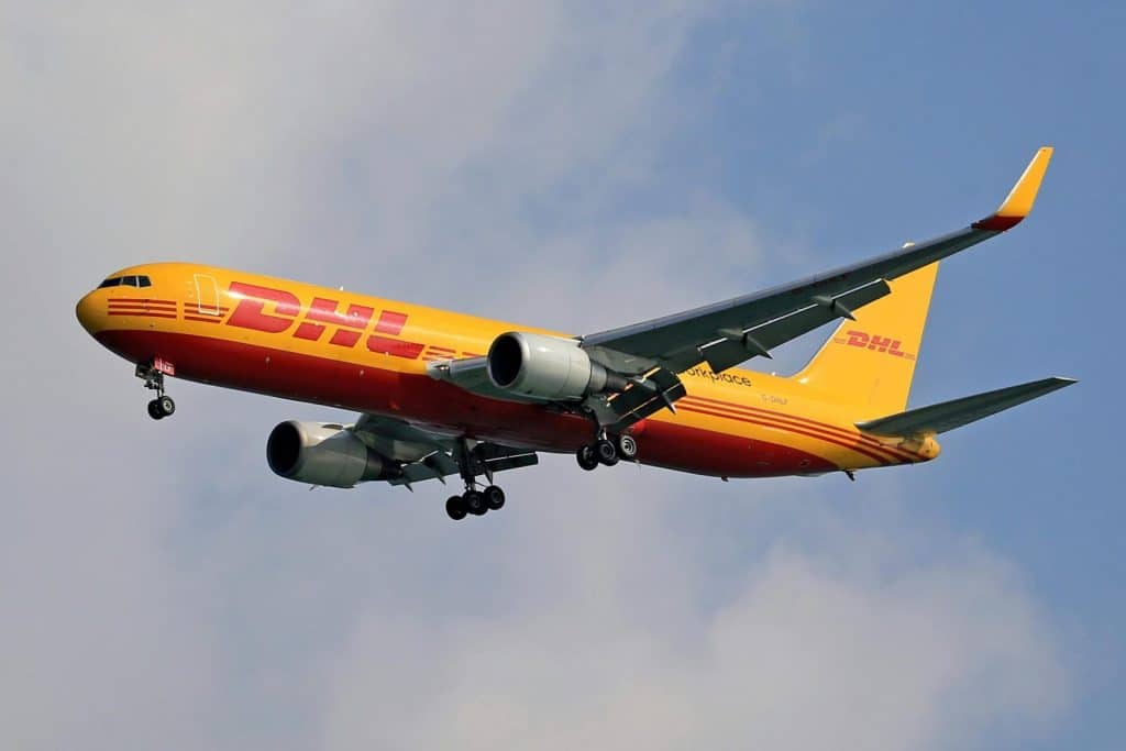 A DHL cargo airplane flying high against a clear blue sky, showcasing logistics and air transport.