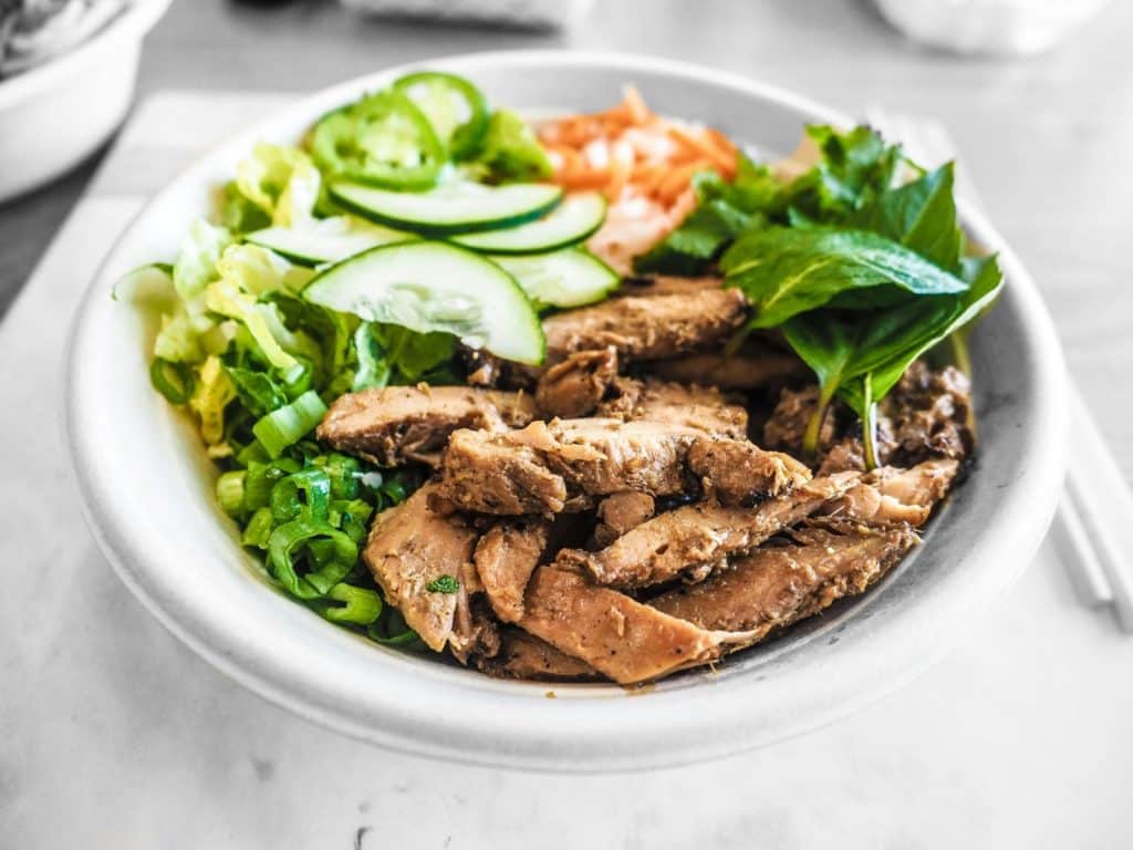 Close-up of a healthy bowl featuring grilled chicken, fresh vegetables, and herbs, perfect for a nutritious meal.