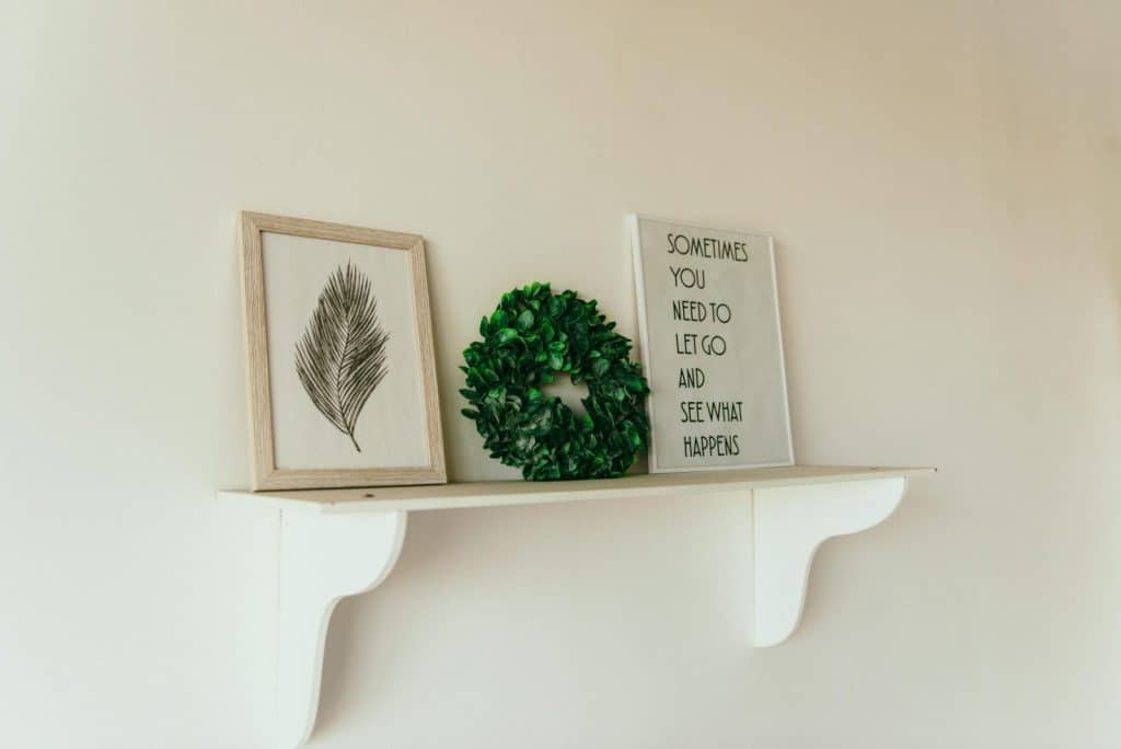 A minimalist shelf with framed art, a green wreath, and an inspirational quote.