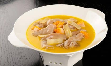 Tasty chicken foot soup with rich broth and vibrant vegetables in a white bowl.