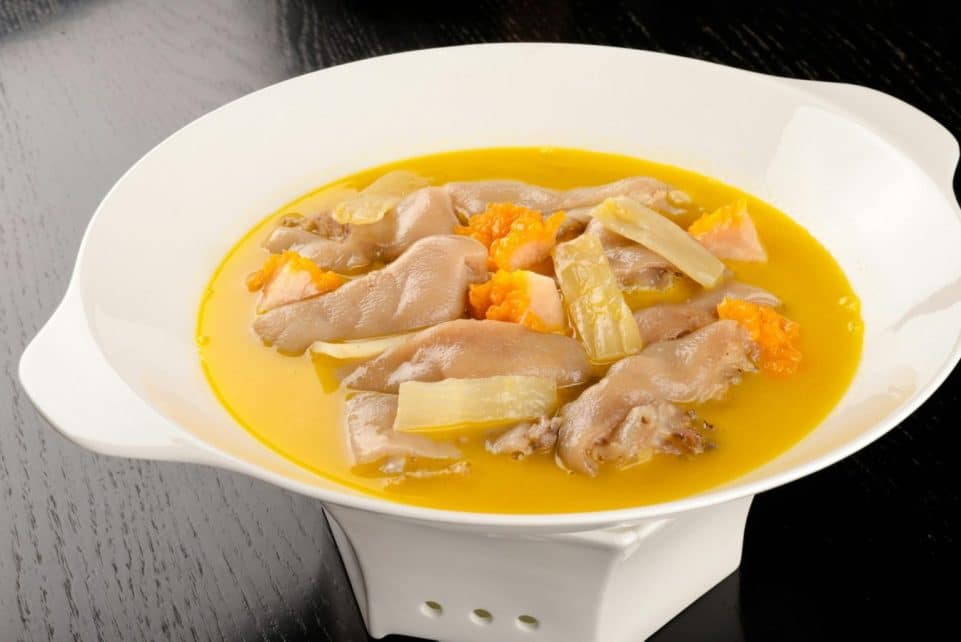 Tasty chicken foot soup with rich broth and vibrant vegetables in a white bowl.