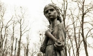 Holodomor memorial statue in Kyiv, Ukraine, depicting a solemn girl in autumn park.