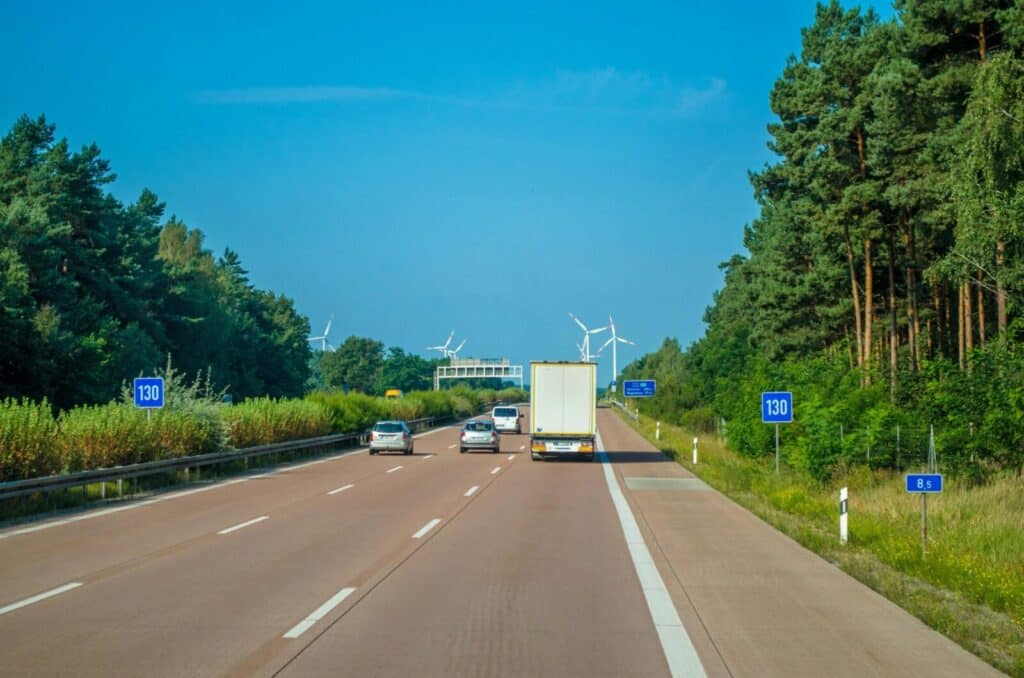 Cars and trucks driving on a highway surrounded by lush greenery and wind turbines.
