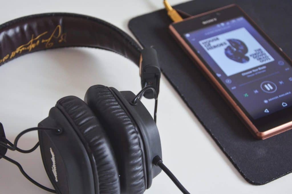 A close-up of headphones and a smartphone playing music on a desk.