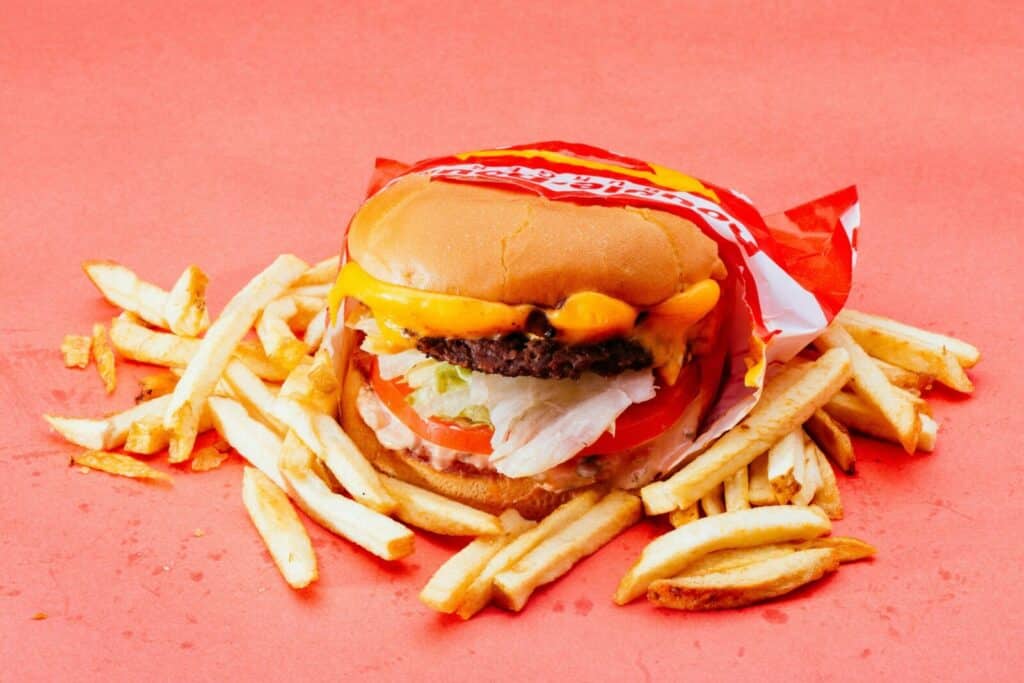 Tasty cheeseburger with fresh ingredients and french fries on a vibrant red background.