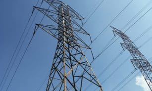 Low angle view of towering electrical transmission lines and pylons under a clear blue sky, conveying energy and electricity concepts.