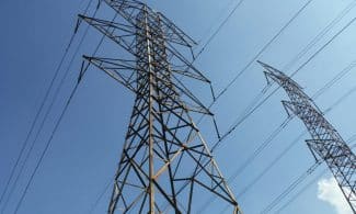 Low angle view of towering electrical transmission lines and pylons under a clear blue sky, conveying energy and electricity concepts.
