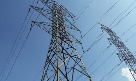 Low angle view of towering electrical transmission lines and pylons under a clear blue sky, conveying energy and electricity concepts.