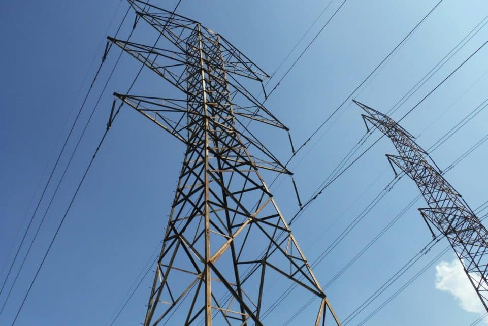 Low angle view of towering electrical transmission lines and pylons under a clear blue sky, conveying energy and electricity concepts.
