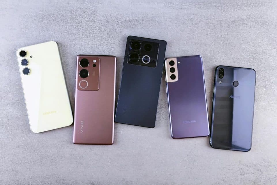 Flat lay of five modern smartphones on a gray surface, showcasing various designs.