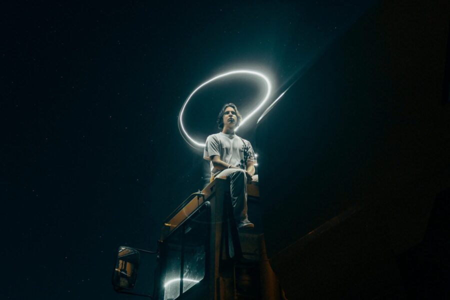 A man sits on a truck, surrounded by a light halo under a starry sky.