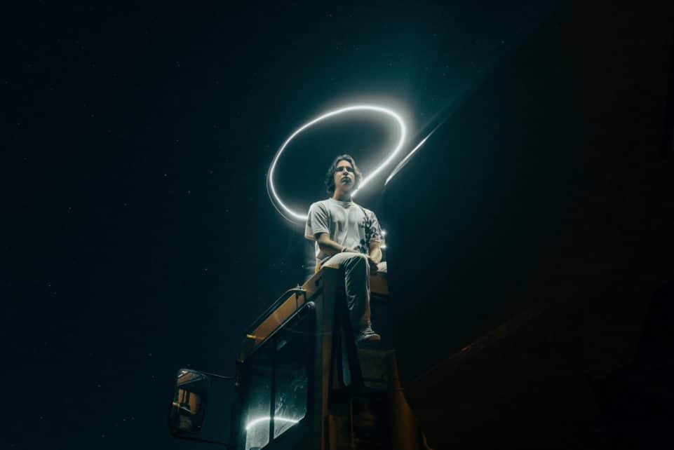 A man sits on a truck, surrounded by a light halo under a starry sky.