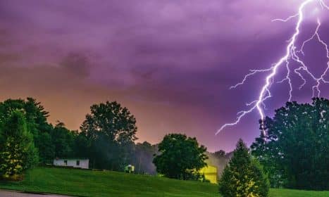 Striking photo capturing a vivid lightning bolt during a storm over a lush green landscape.
