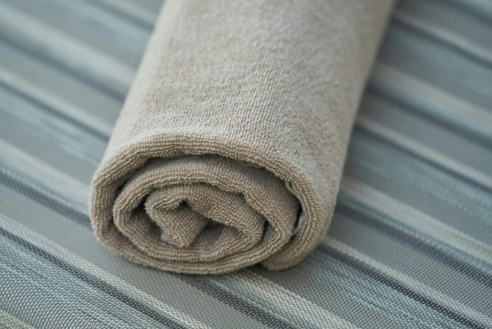 Close-up of a soft beige cotton towel rolled neatly on a striped fabric surface. Perfect for home decor or textile themes.