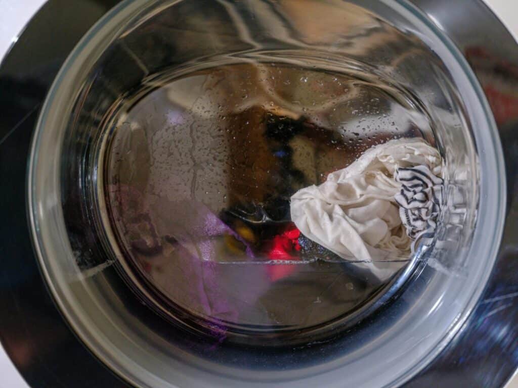 A clear view of wet clothes spinning inside a front-loading washing machine.