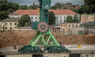 A large green industrial crane at Klaipėda Harbor, Lithuania, amidst a backdrop of buildings and trees.