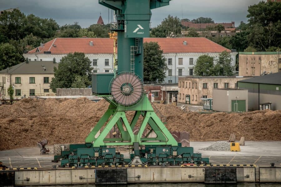 A large green industrial crane at Klaipėda Harbor, Lithuania, amidst a backdrop of buildings and trees.