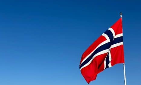 Norwegian flag waving in clear blue sky, symbolizing patriotism and national pride.